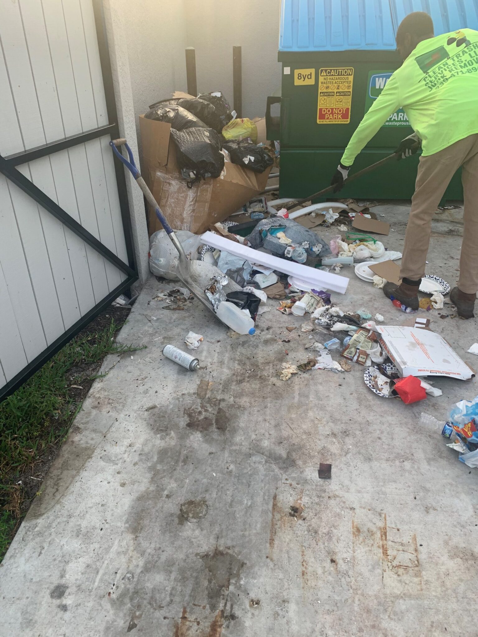 Employee raking up trash to throw in into dumpster.